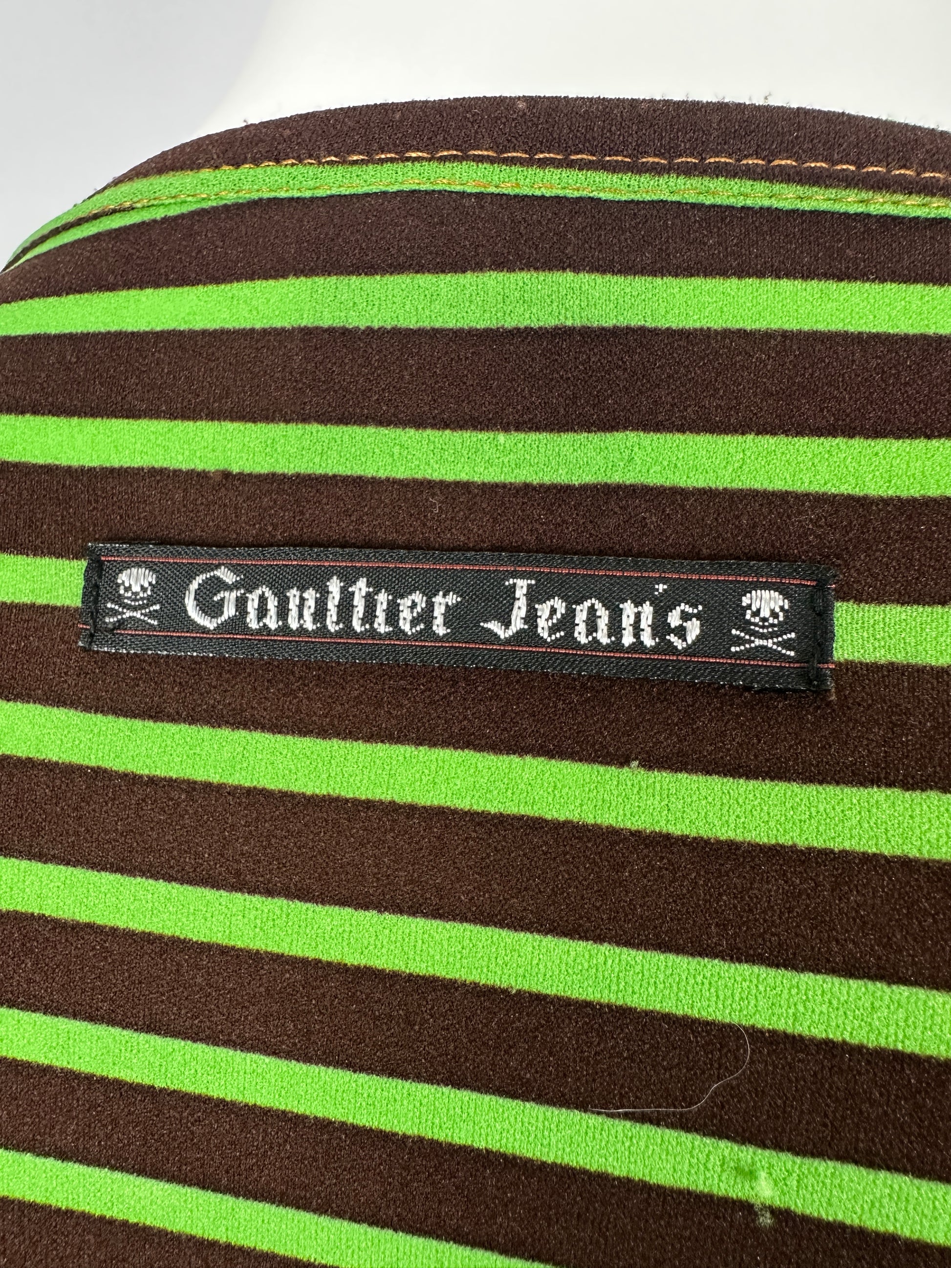 Close-up of a Gaultier Jeans label on a brown and green striped fabric.