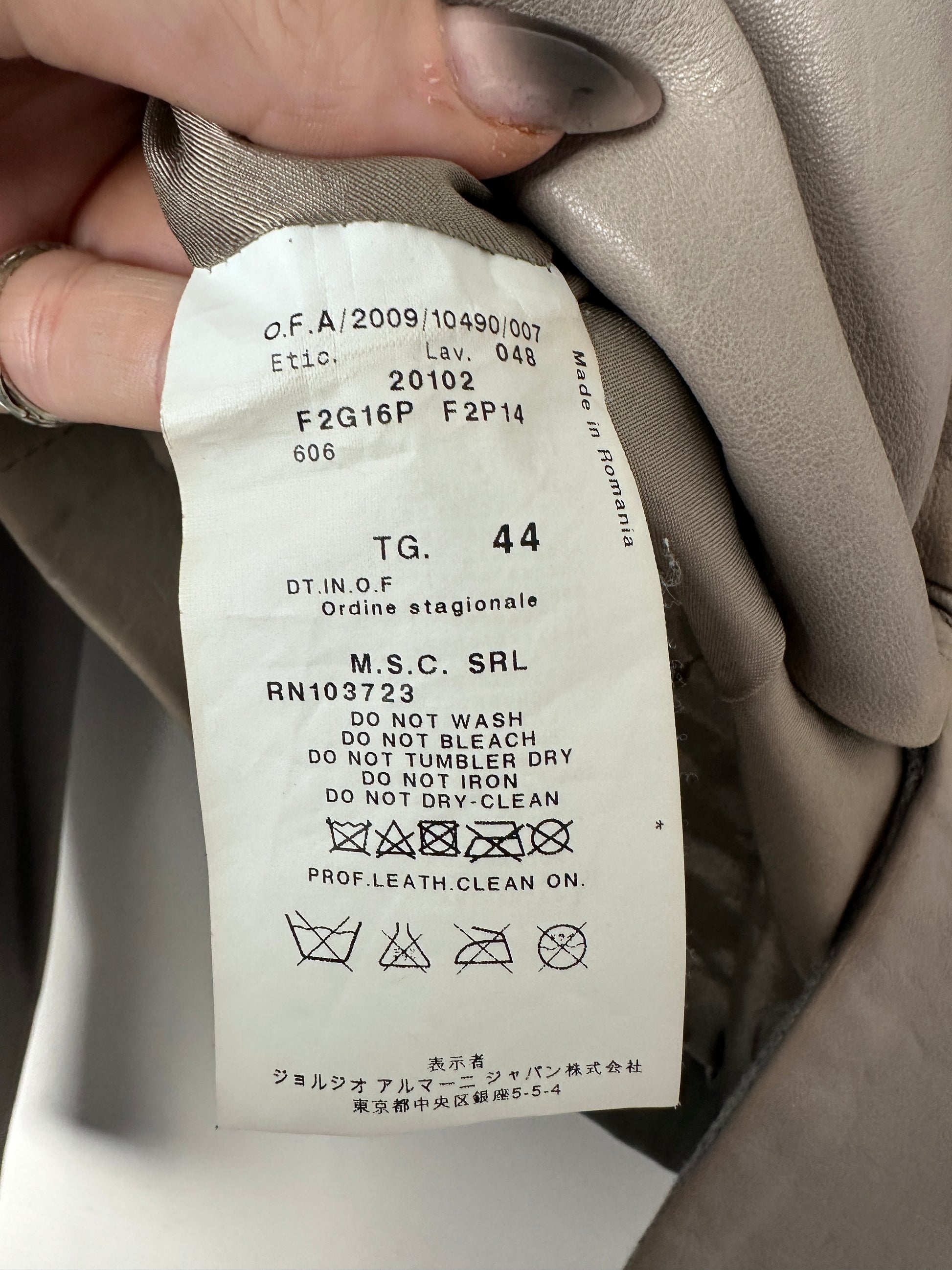 Close-up of a clothing label on a beige garment with visible text and symbols.