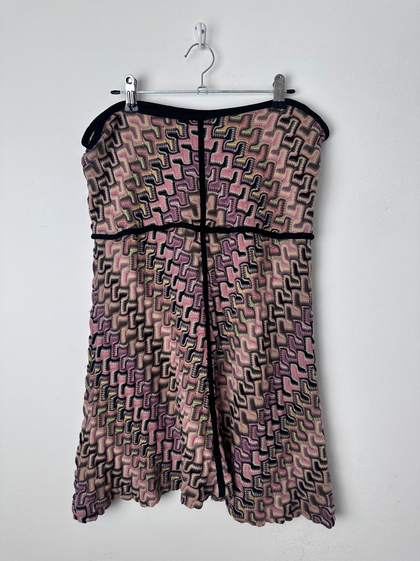 A patterned knit garment laid flat on a white background, hanging from a clear plastic hanger. The fabric has an abstract geometric maze-like pattern in dusty pink, mauve, black, and gray, with solid black trim.